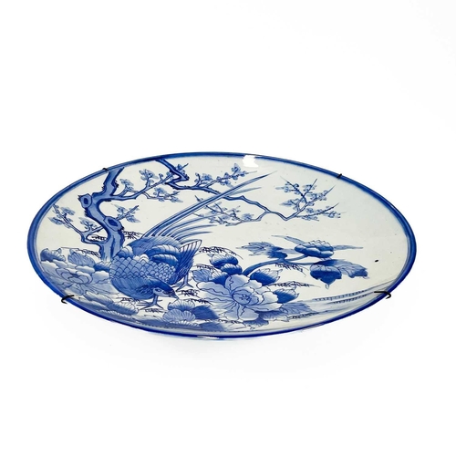 811 - A Japanese Arita blue and white charger. Circa 1900, painted with a pheasant beside a prunus tree an... 