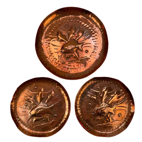 102 - A suite of three Newlyn copper dishes. Each repousse decorated with fish and seaweed on a planished ... 