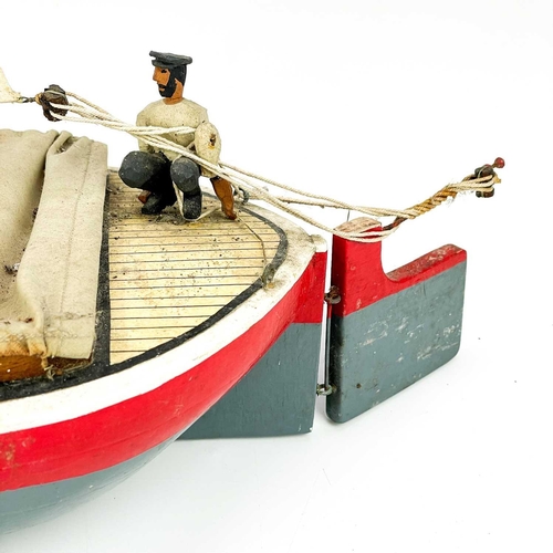 200 - A painted model of a sailing boat. Mounted a painted figure of a fisherman, length 53cm.