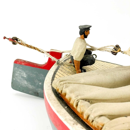 200 - A painted model of a sailing boat. Mounted a painted figure of a fisherman, length 53cm.