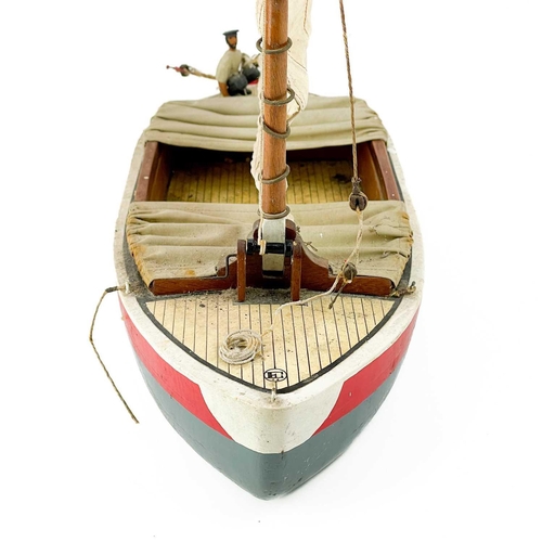 200 - A painted model of a sailing boat. Mounted a painted figure of a fisherman, length 53cm.