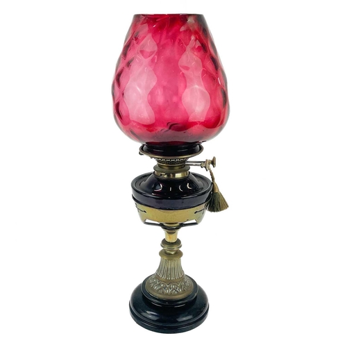 205 - A Victorian brass oil lamp with a cranberry glass shade. Raised on a circular base, with a glass oil... 