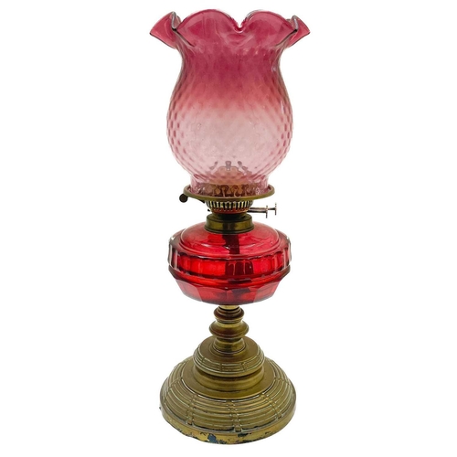 26 - A Victorian brass oil lamp with a cranberry glass shade. Raised on a circular base, with a cranberry... 