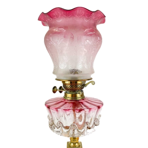 47 - A Victorian brass oil lamp with a glass oil reservoir and cranberry shade. With corinthian style bra... 