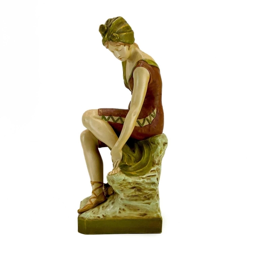 531 - A Royal Dux figure of a bather. Early 20th century, wearing a coloured swimsuit and seated on a rock... 