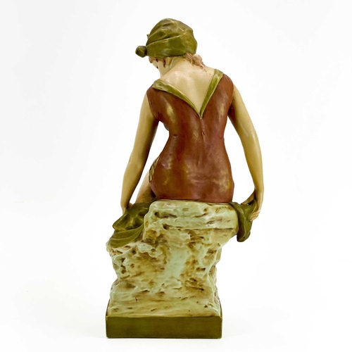 531 - A Royal Dux figure of a bather. Early 20th century, wearing a coloured swimsuit and seated on a rock... 