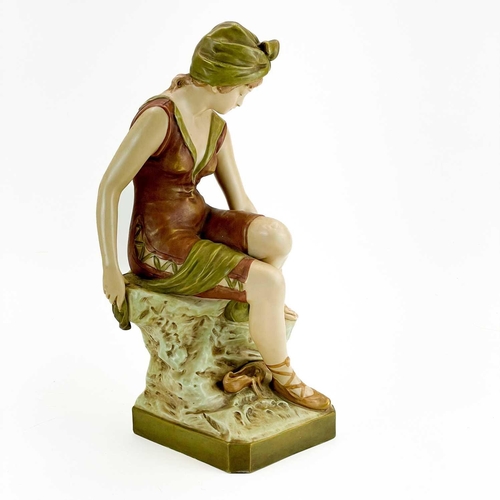 531 - A Royal Dux figure of a bather. Early 20th century, wearing a coloured swimsuit and seated on a rock... 