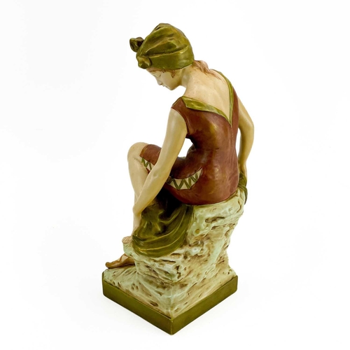 531 - A Royal Dux figure of a bather. Early 20th century, wearing a coloured swimsuit and seated on a rock... 