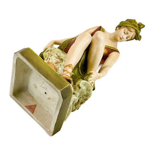 531 - A Royal Dux figure of a bather. Early 20th century, wearing a coloured swimsuit and seated on a rock... 