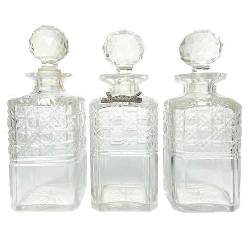 589 - A set of three cut glass decanters and faceted stoppers. One with a silver Whisky label, together wi... 