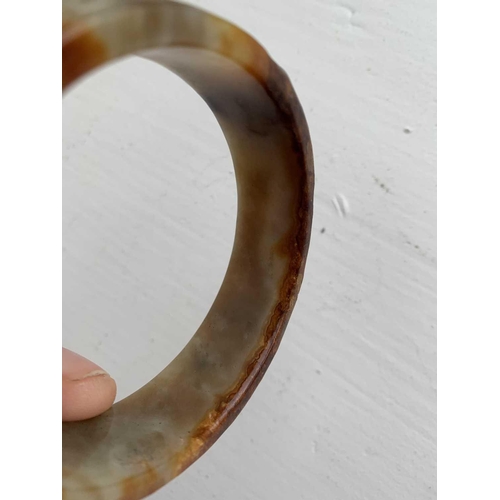 22 - A Chinese carved jade bangle, probably Neolithic period. With russet inclusions, carved with opposin... 