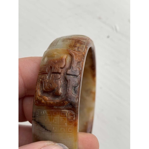 22 - A Chinese carved jade bangle, probably Neolithic period. With russet inclusions, carved with opposin... 