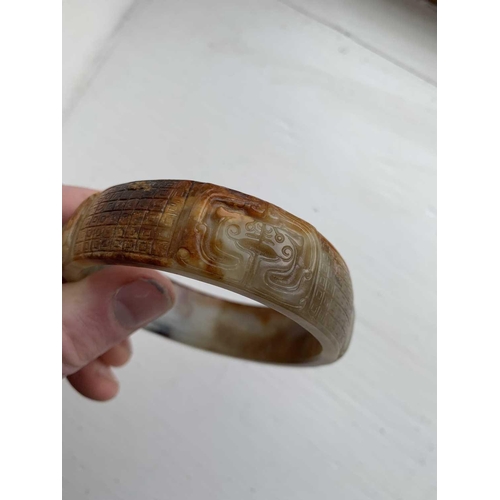 22 - A Chinese carved jade bangle, probably Neolithic period. With russet inclusions, carved with opposin... 