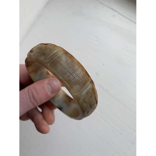 22 - A Chinese carved jade bangle, probably Neolithic period. With russet inclusions, carved with opposin... 