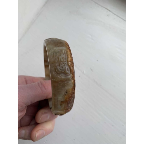 22 - A Chinese carved jade bangle, probably Neolithic period. With russet inclusions, carved with opposin... 