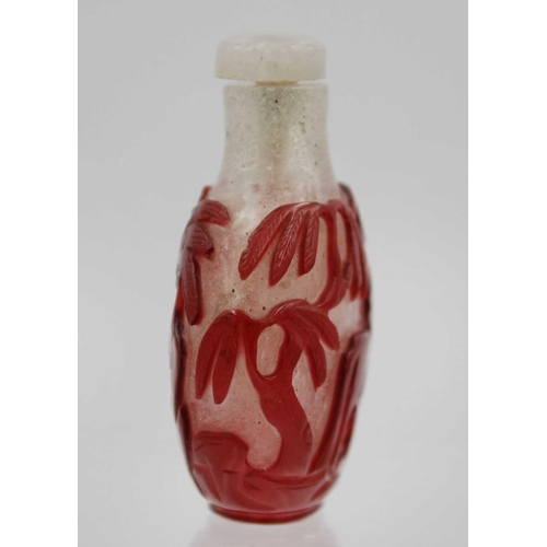 244 - A Chinese red overlay glass snuff bottle. With hardstone stopper, the body depicting horses below wi... 