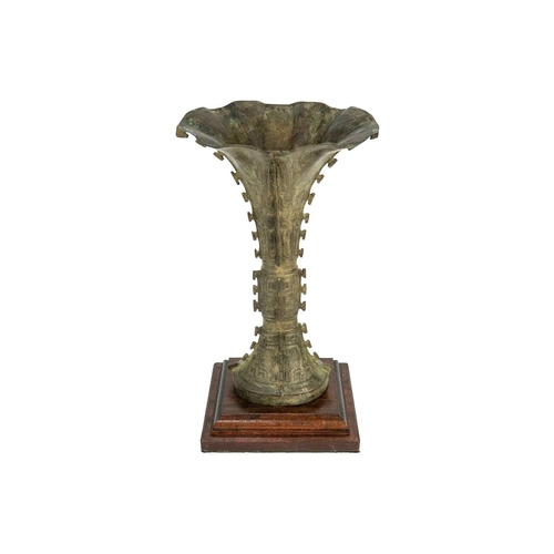 93 - A Chinese bronzed metal Gu vase. With flared trumpet rim and of archaic form, on a later wooden base... 