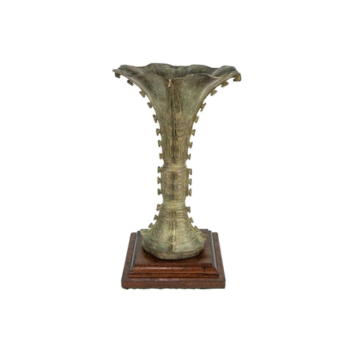 93 - A Chinese bronzed metal Gu vase. With flared trumpet rim and of archaic form, on a later wooden base... 