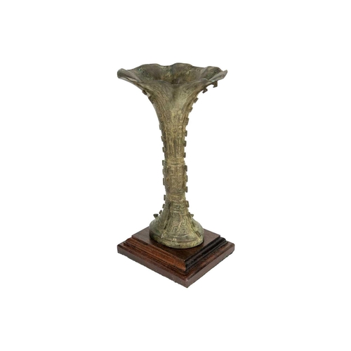 93 - A Chinese bronzed metal Gu vase. With flared trumpet rim and of archaic form, on a later wooden base... 