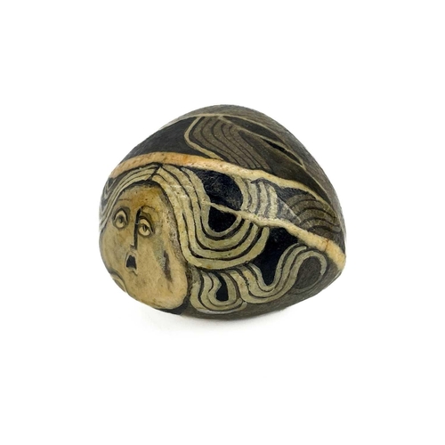 42 - Irene Jones (1938) A pebble painted with a female mask, signed and dated '74, length 5cm, together w... 