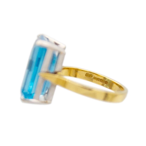 65 - An 18ct yellow and white gold, blue topaz set cocktail ring. The rectangular step cut topaz of 10.6c... 