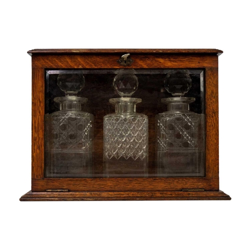 26 - An oak glazed tantalus circa 1900. With bevel glazed fall front door, height 27cm width 36.5cm depth... 