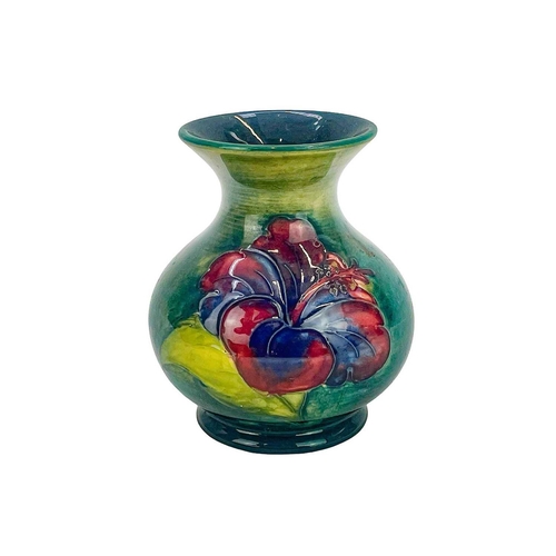 554 - A Walter Moorcroft hibiscus small vase. The flowers painted on a mottled green ground, height 9.5cm,... 