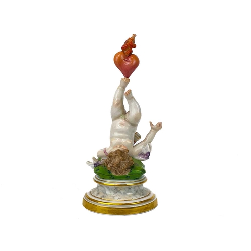 776 - A Meissen figure of Cupid balancing a flaming heart on his foot. Early 20th century, his shoulders r... 