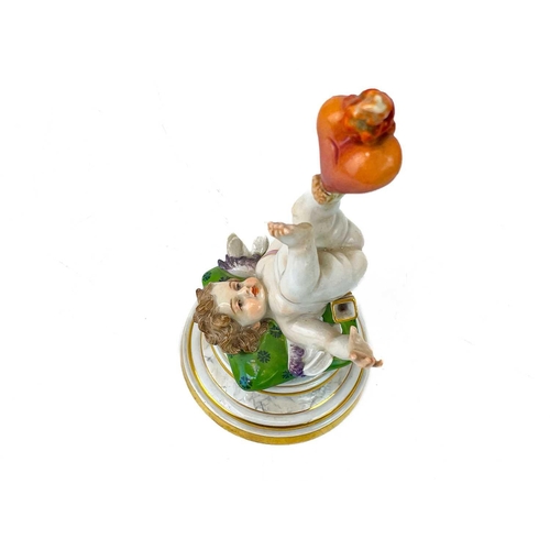 776 - A Meissen figure of Cupid balancing a flaming heart on his foot. Early 20th century, his shoulders r... 