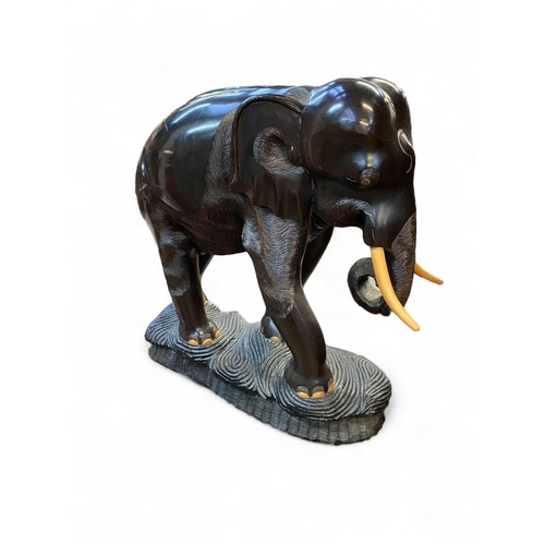 111 - A carved ebonised wood elephant figure Of large proportions, with softwood tusks and a carved base, ... 