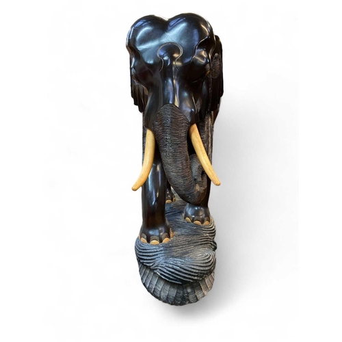 111 - A carved ebonised wood elephant figure Of large proportions, with softwood tusks and a carved base, ... 