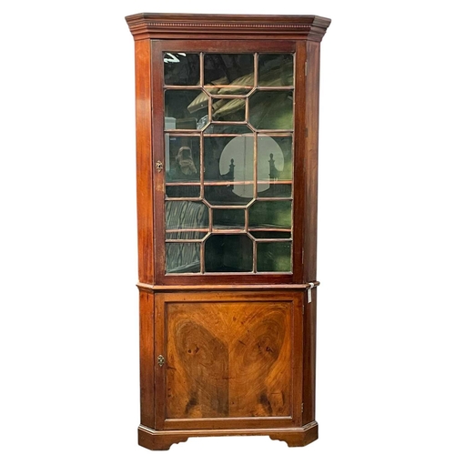 702 - A 19th century mahogany floor standing corner cupboard. The upper part with a glazed door enclosing ... 