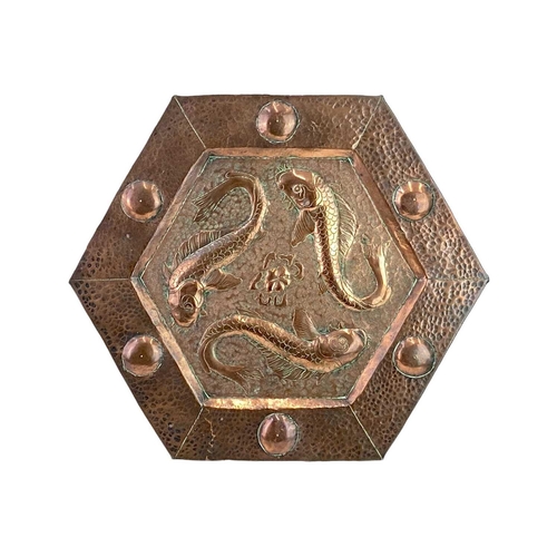 92 - An arts and crafts hexagonal copper plaque. Repousse decorated with three fish, the planished border... 