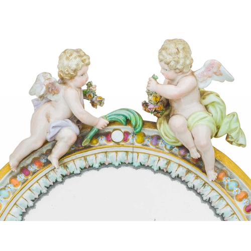 202 - A Meissen oval porcelain easel mirror. Circa 1880, surmounted by two winged cherubs and with a colou... 