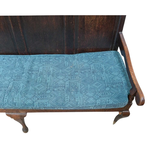 444 - An oak settle with a quadruple fielded panel back. On cabriole front legs, with a loose seat cushion... 