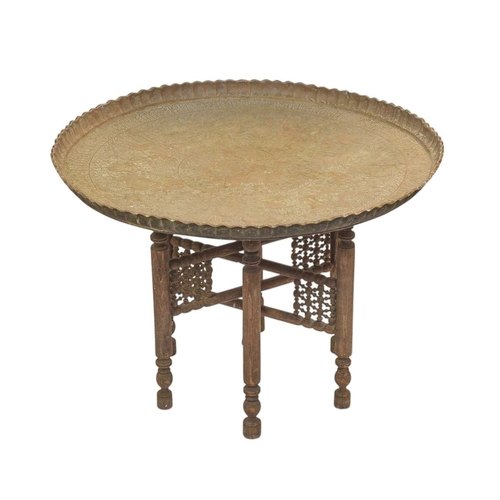 498 - An Indian circular brass table on a folding wooden stand. The tray decorated with embossed figures a... 