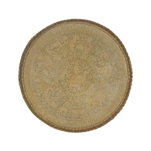 498 - An Indian circular brass table on a folding wooden stand. The tray decorated with embossed figures a... 