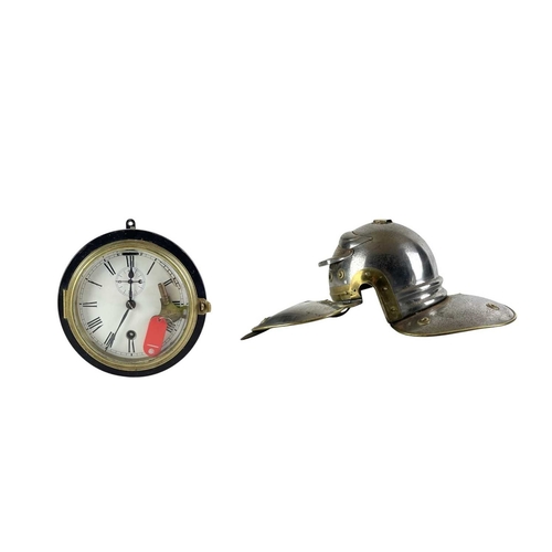 64 - A painted and brass mounted bulkhead wall clock and a Roman style helmet. The former with a white en... 