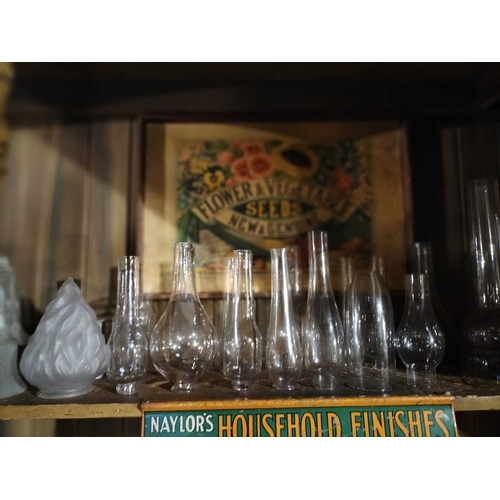 117 - ± Clemence's Ironmongers Glass lamp shades and oil lamp chimneys The top shelf contents to include m... 