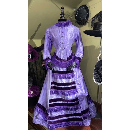 605 - ± K Fillingham Milliners A mannequin wearing a purple silk Victorian day dress A black fabric covere... 