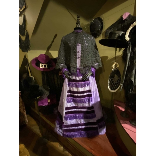 605 - ± K Fillingham Milliners A mannequin wearing a purple silk Victorian day dress A black fabric covere... 