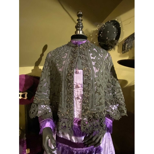 605 - ± K Fillingham Milliners A mannequin wearing a purple silk Victorian day dress A black fabric covere... 