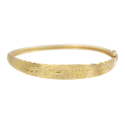 145 - A 9k oval hinged bangle with leaf-cut decoration. Stamped 375, width 64mm, 6.5g.