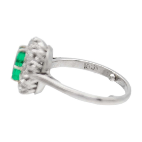 30 - An emerald and diamond set white gold cluster ring. A rectangular step-cut, vivid, saturated green e... 