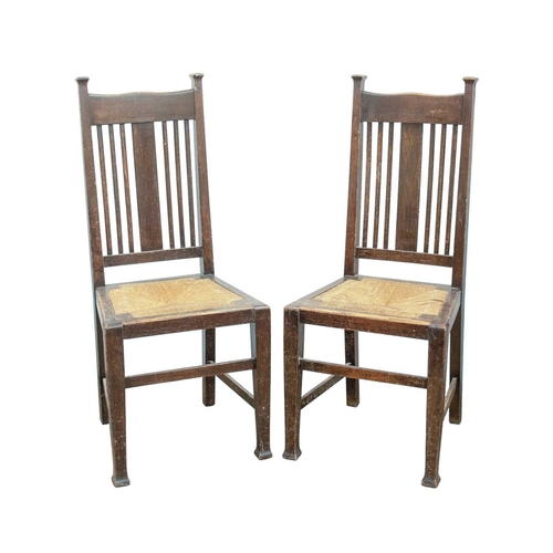 205 - A pair of Arts and Crafts oak dining chairs. To a design by Charles Voysey, with shaped top rails, v... 