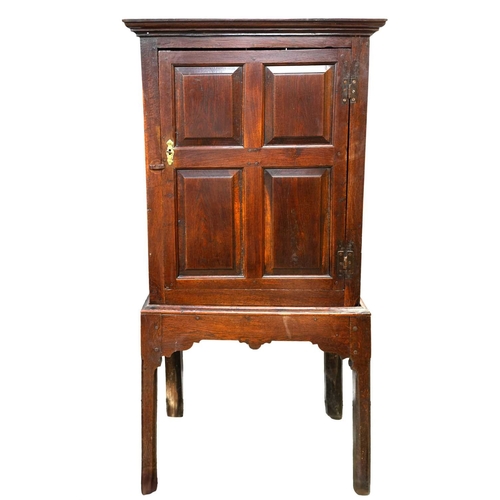 690 - An 18th century oak cupboard on stand. The single door with four neat panels with moulded edges, the... 