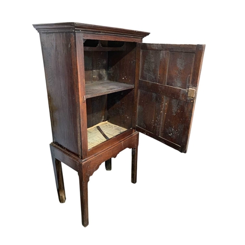 690 - An 18th century oak cupboard on stand. The single door with four neat panels with moulded edges, the... 