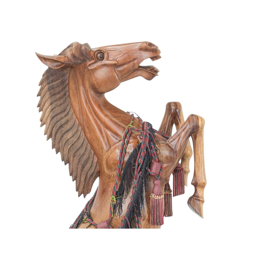 102 - A large carved hardwood figure of a rearing stallion. Late 20th century, standing on a naturalistic ... 