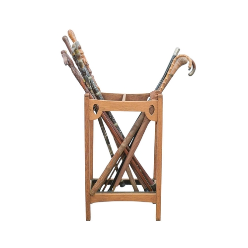 23 - A collection of walking sticks and canes in an Art Nouveau oak stand. Including two silver topped eb... 