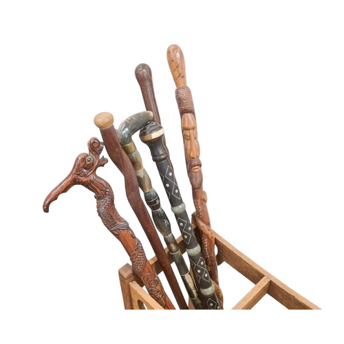 23 - A collection of walking sticks and canes in an Art Nouveau oak stand. Including two silver topped eb... 